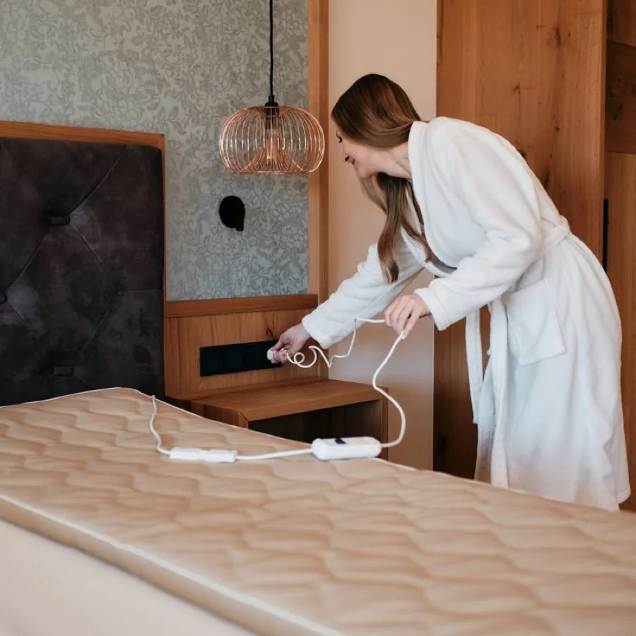 The pad lies on the bed and is plugged in