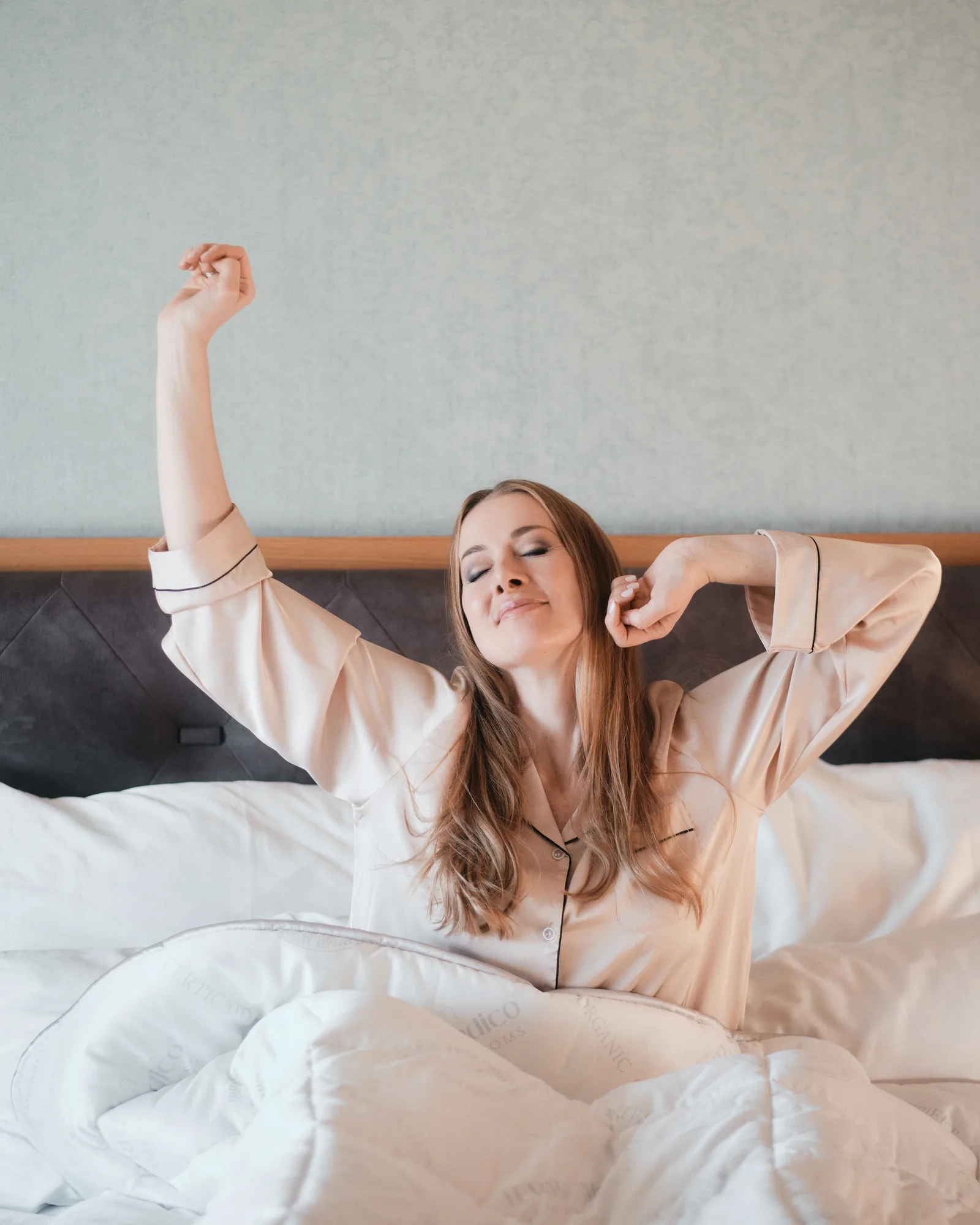 Frau streckt sich beim Aufwachen im Bett, Stimmungsbild zu erholtem Schlaf mit BETTER³